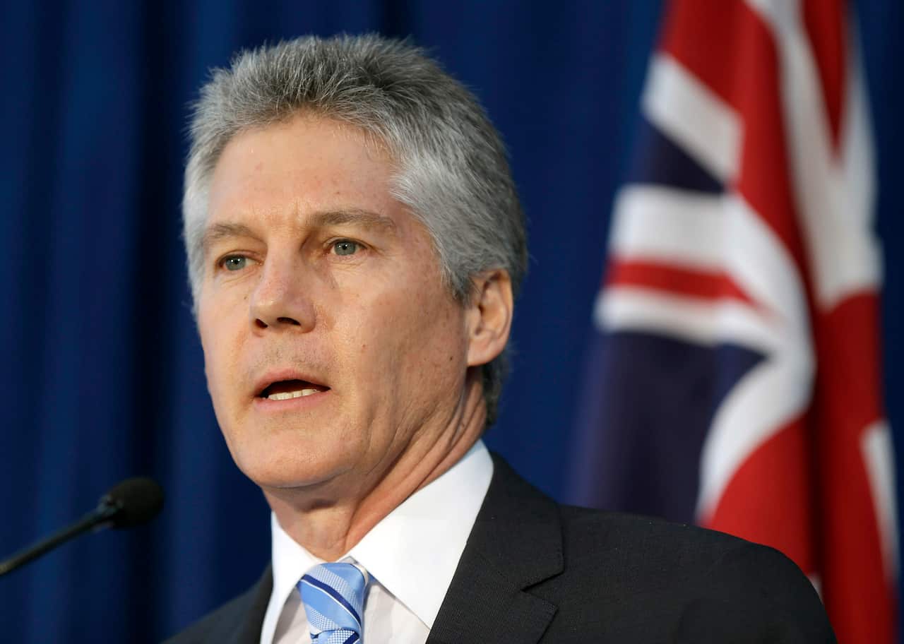 A man speaking into a microphone. An Australian flag is behind him.