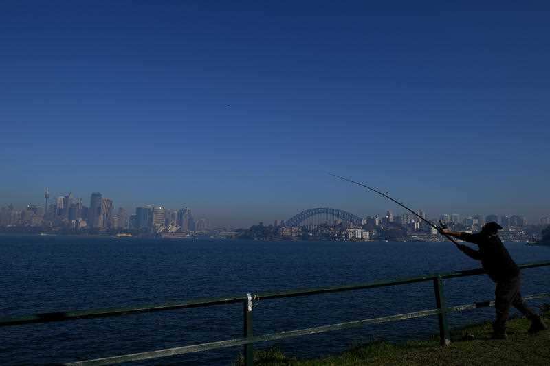 A fisherman casts his line as smoke is seen blanketing the Sydney city skyline as a result of Rural Fire Service hazard reduction burn.