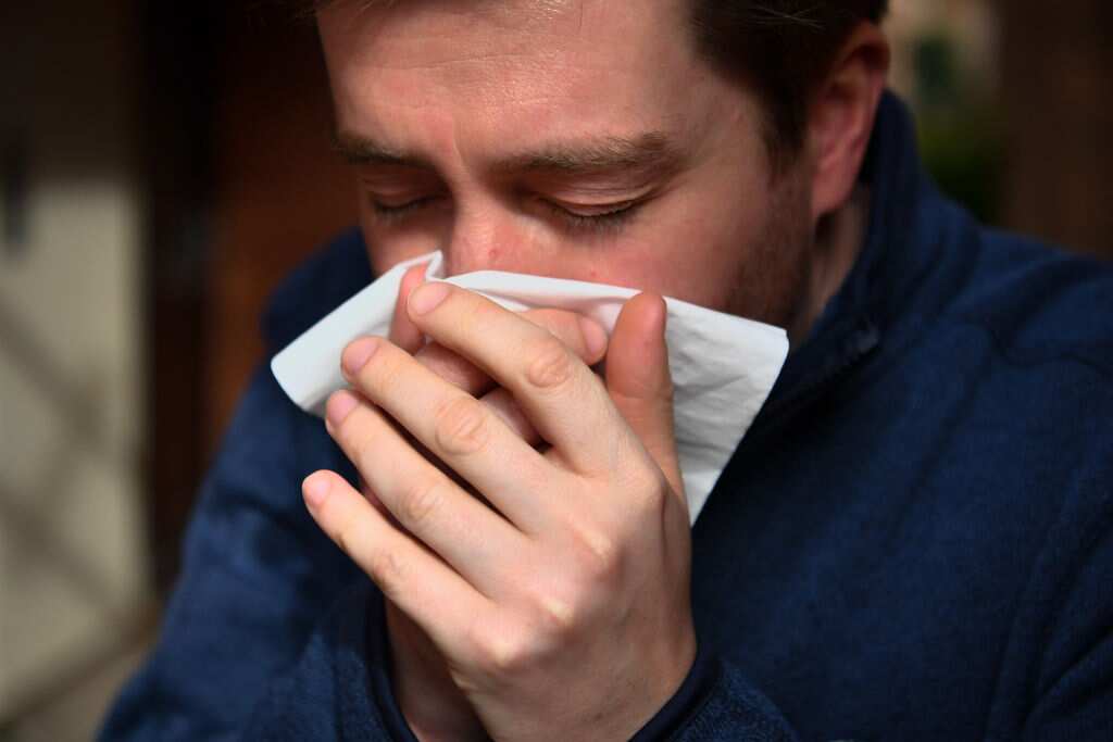A man sneezes into a tissue. 