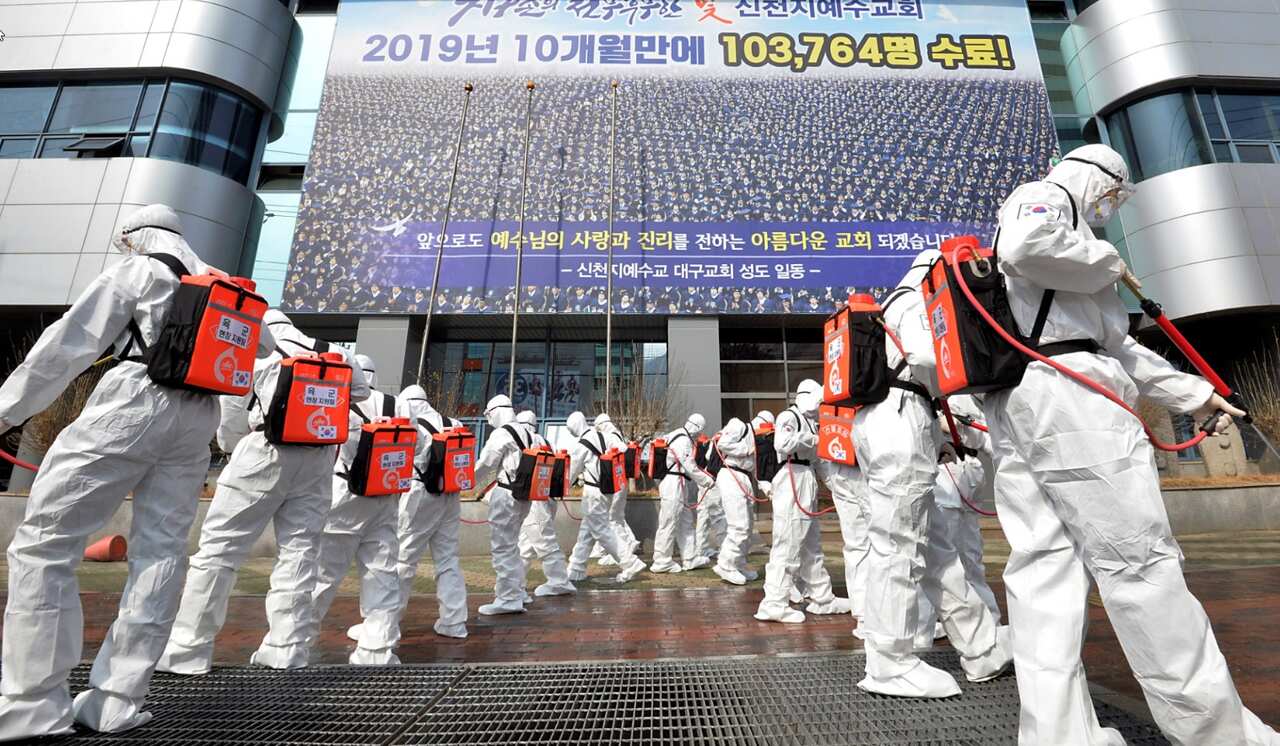 Army soldiers wearing protective suits spray disinfectant to prevent the spread of the coronavirus in front of a branch of the Shincheonji Church of Jesus.