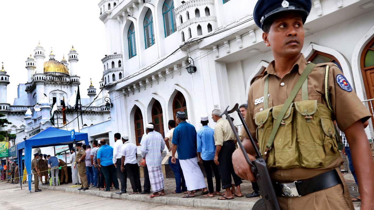 Sri Lankan security forces stand guard while Muslim people queue up for security outside Dawatagaha mosque at Town Hall in Colombo.