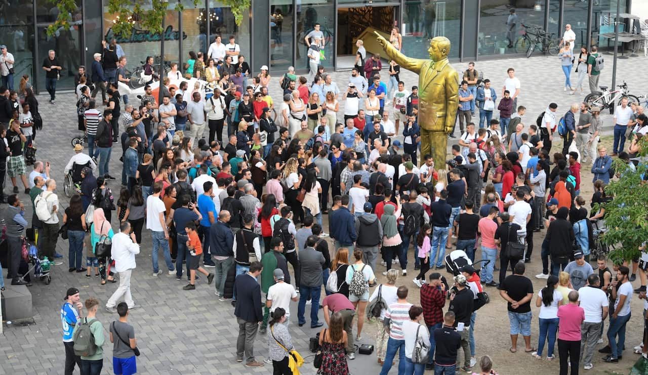 People gather around a golden statue of Turkish President Recep Tayyip Erdogan stands on the Square of German Unity in Wiesbaden.