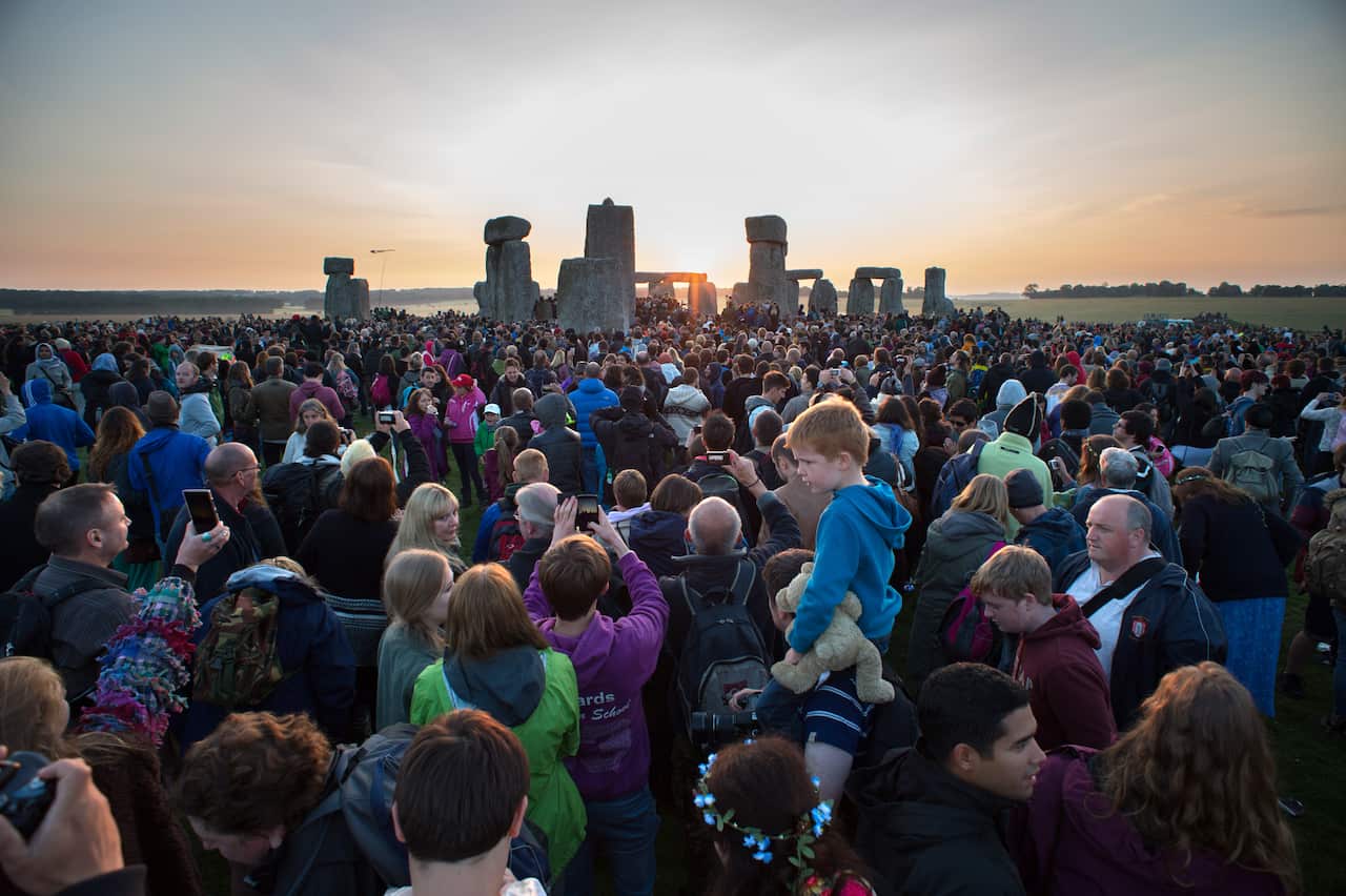 Large group of people gathered around Stonehenge at sunrise.