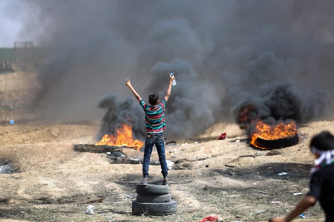 A Palestinian flashes the V-sign in front of burning tyres along the border with the Gaza strip.