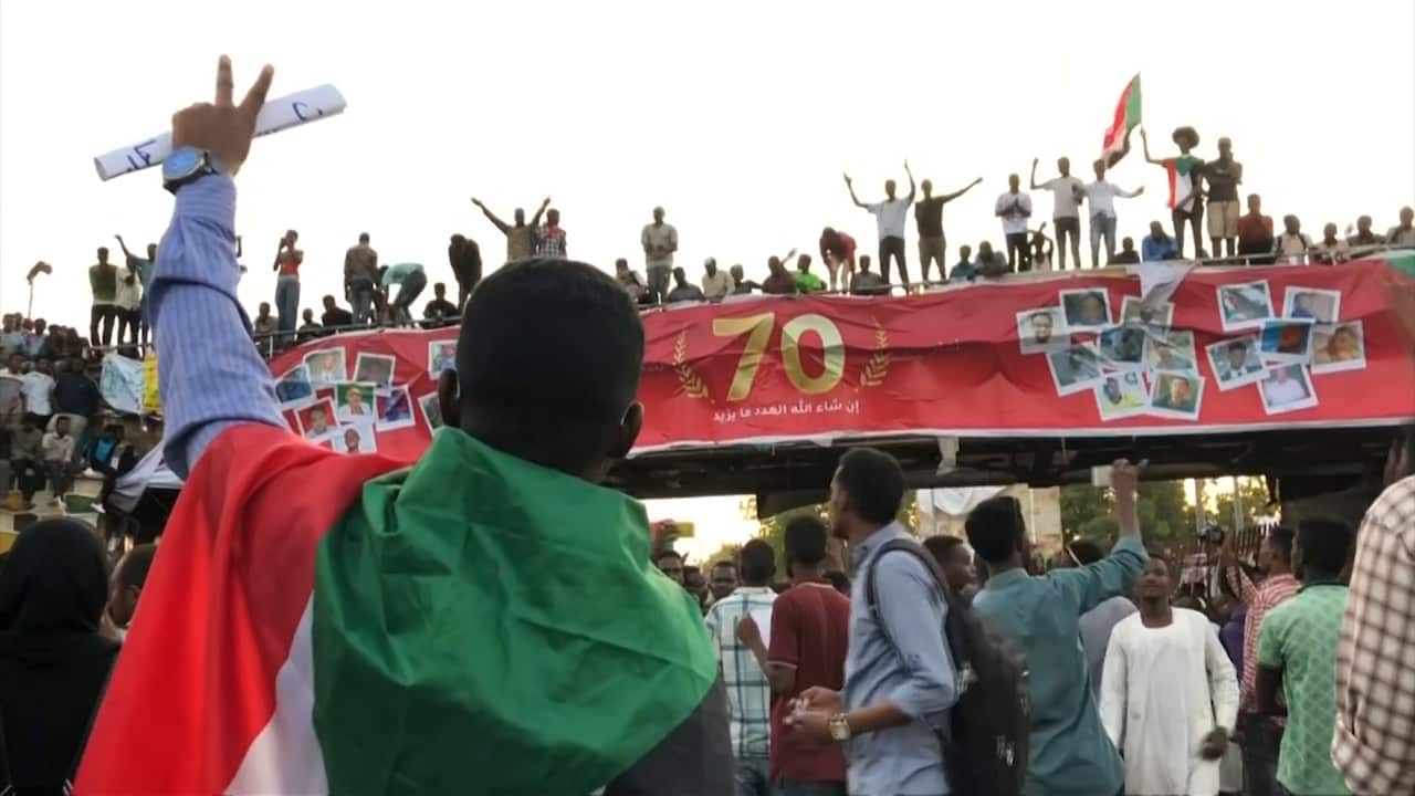 man giving the peace sign in front of pretestors 