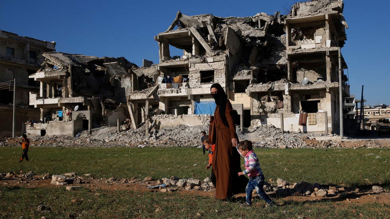 Syrian woman with her kids walks in front of buildings destroyed during fighting in Manbij.