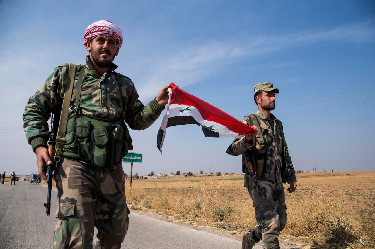 Syrian government forces carry a national flag as they man a checkpoint near the town of Tal Tamr, north Syria.