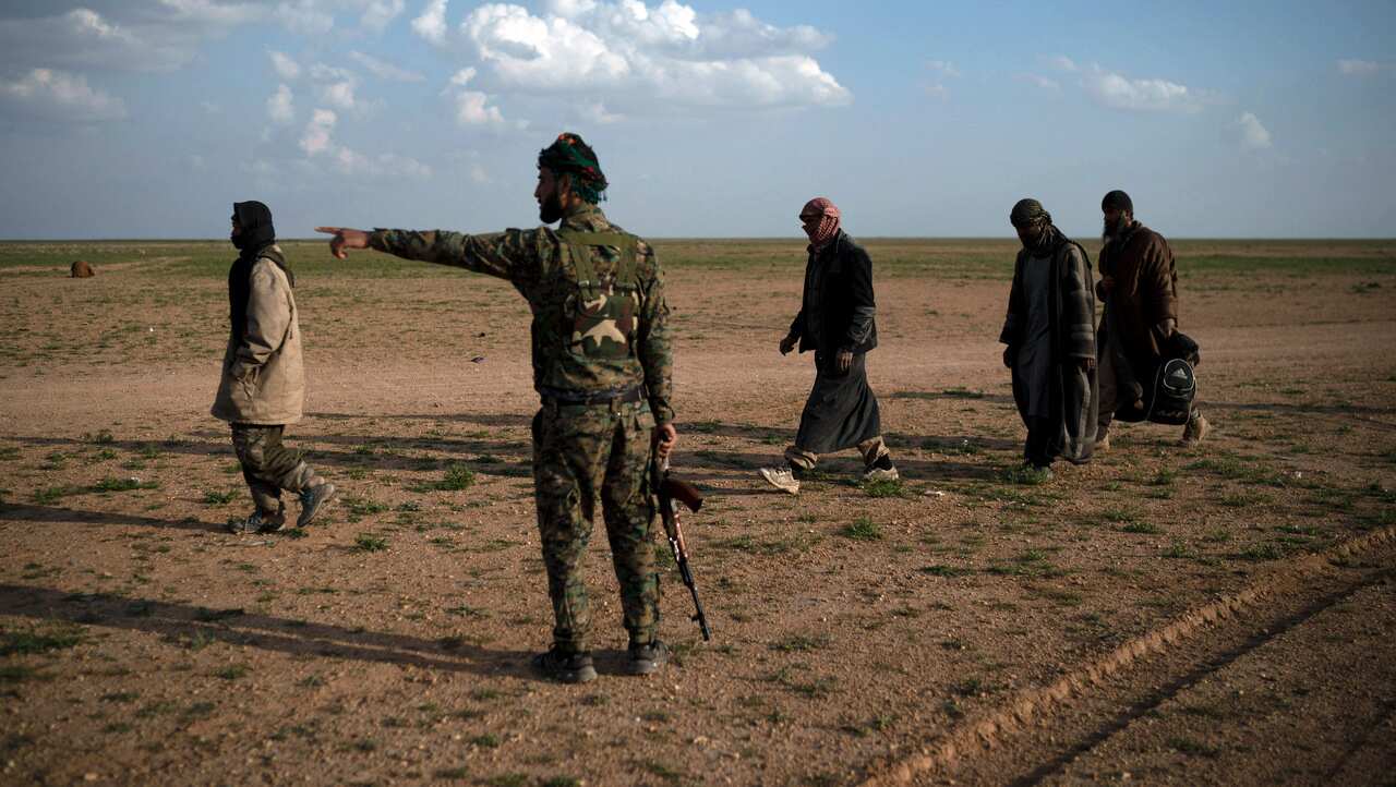 A US-backed Syrian Democratic Forces (SDF) fighter gestures as men walk to be screened after being evacuated out of the last territory held by IS, near Baghouz.