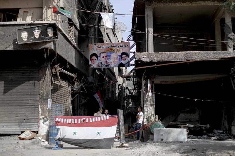 Men sit under a poster of the late Iranian revolutionary founder Ayatollah Khomeini and Syrian President Bashar Assad in the Syrian capital Damascus.