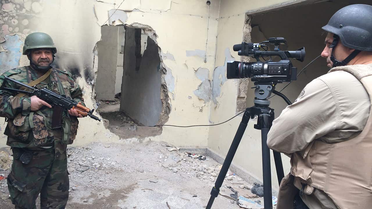 Luke films in Syria with Colonel Ahmed Zarqa in a damaged building.