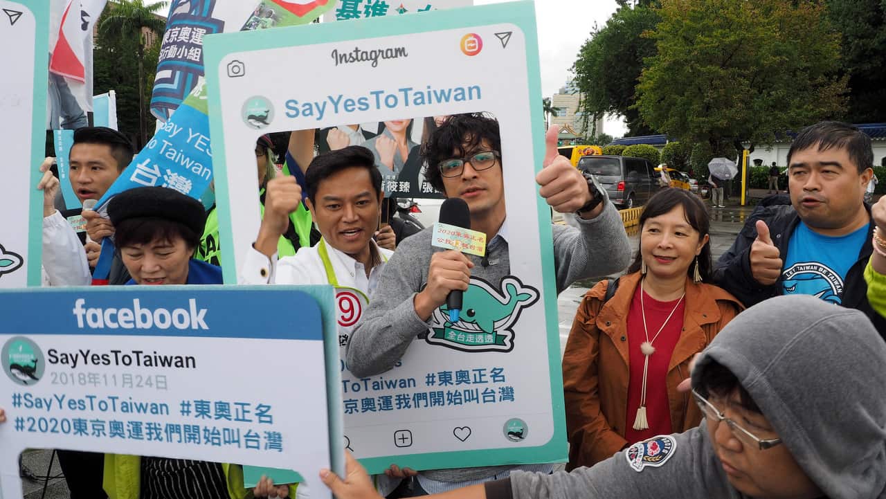 Taiwanese people holding frames reading 'Say Yes To Taiwan' and 'Call Us Taiwan at Tokyo Olympics'.