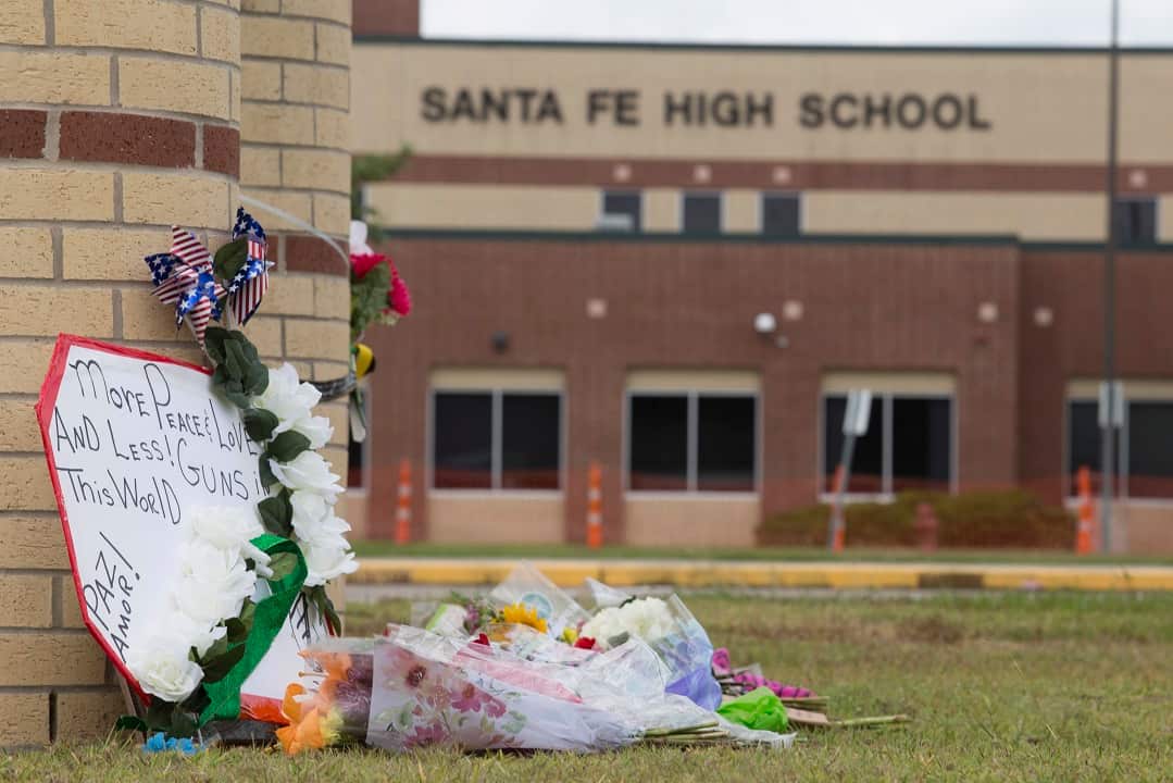 A sign is seen propped against a wall with flowers on the ground in front of it.