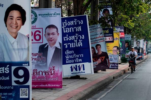 A woman rides a bicycle past electoral posters in Bangkok.