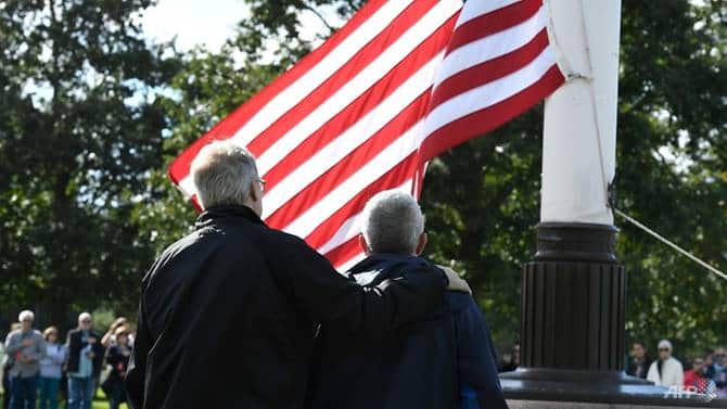 Half-brothers look on as the US flag is raised in the grounds of the Normandy American Cemetery and Memorial at Colleville-sur-Mer where their father landed.