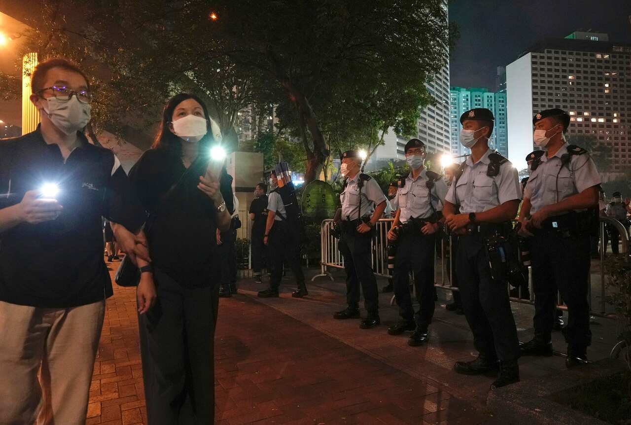People hold candles walk past police officers near Hong Kong Victoria Park on 4 June 2021.
