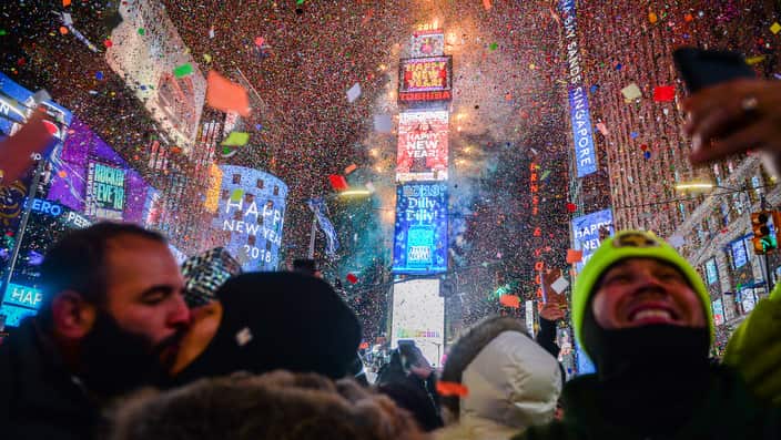 People celebrate New Year as confetti falls. Tall buildings lit wit neon signs are in the background