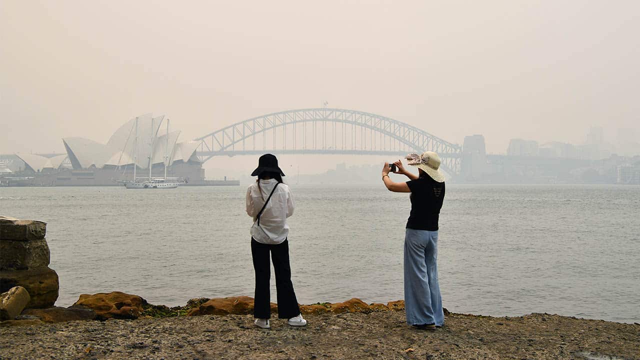Tourists snap a photo of a smoke-filled Sydney Harbour. Tourists are staying away due to the bushfires. 