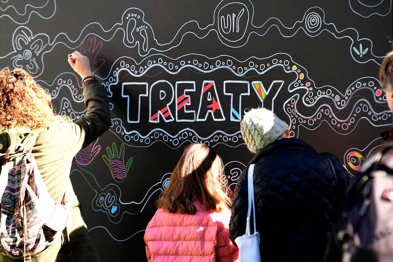 People are seen drawing their hand onto communal art boards at The City of  annual NAIDOC in the City event.