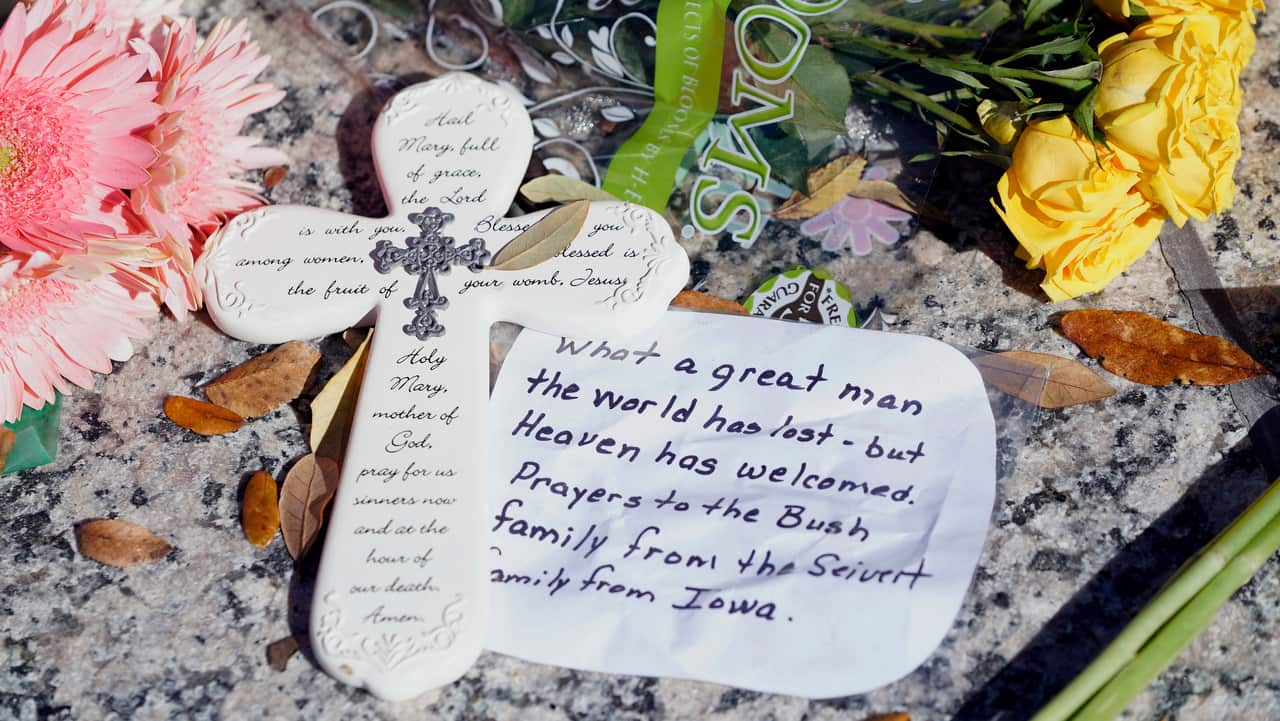A messages sits among flowers left at the base of a statue of George H.W. Bush outside the George H.W. Bush Presidential Library and Museum.