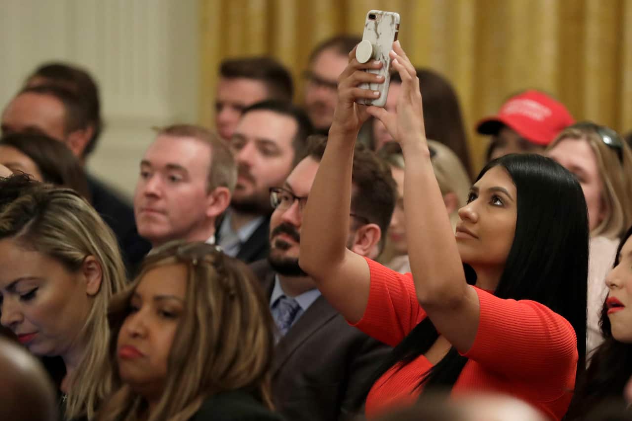 A guest takes a photo as President Donald Trump speaks during the "Presidential Social Media Summit" in the East Room of the White House.