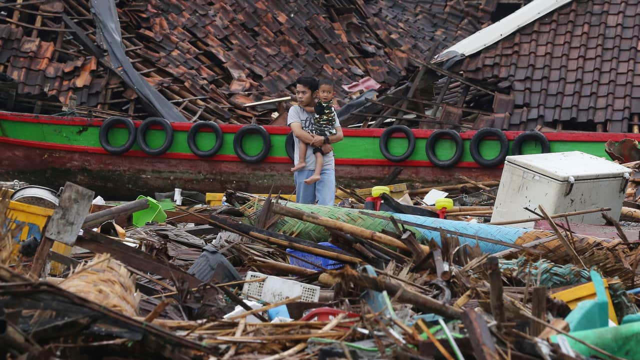A man holding a child looks the damage at a tsunami-ravaged village in Sumur, Indonesia.