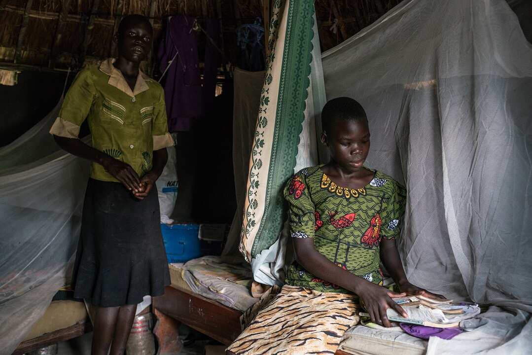 Josephine Bako, 13, right, who was adopted by her aunt, Queen Chandia, not pictured, after her parents died in South Sudan, organizes her schoolbooks in her room in a refugee settlement in Oliji, Uganda.