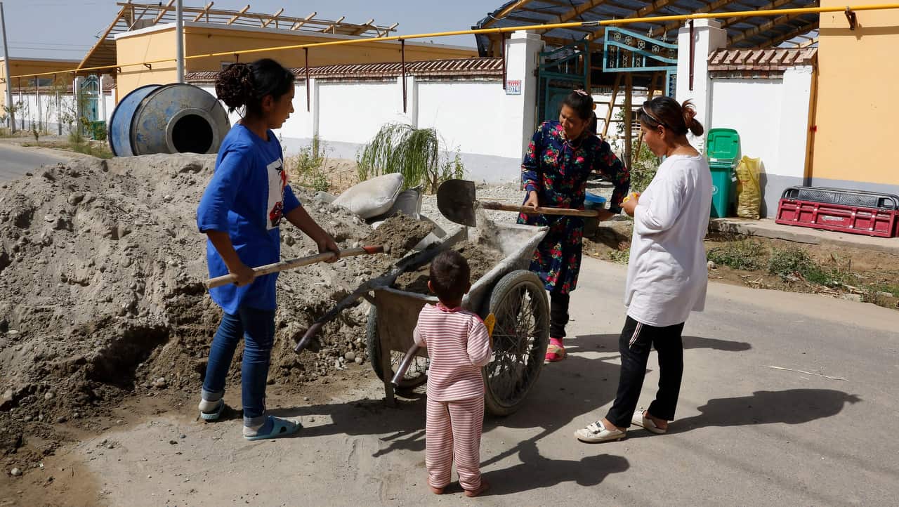 Uighur women use carts to transport cement for home renovations at the Unity New Village in Hotan.
