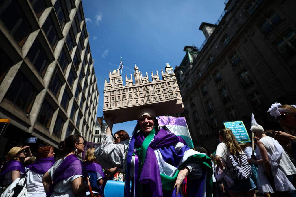 A women wearing a 'Houses of Parliament' model hat reacts as she takes part in mass participation artwork 'Processions'.