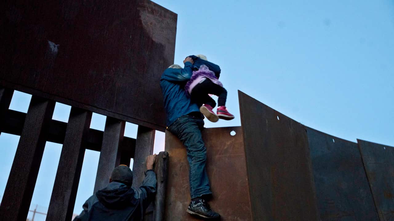 A Honduran migrant helps a young girl cross to the American side of the border wall, in Tijuana, Mexico.