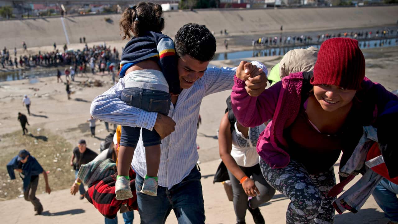 Migrants walk up a riverbank at the Mexico-US border after getting past a line of Mexican police at the Chaparral border crossing in Tijuana.