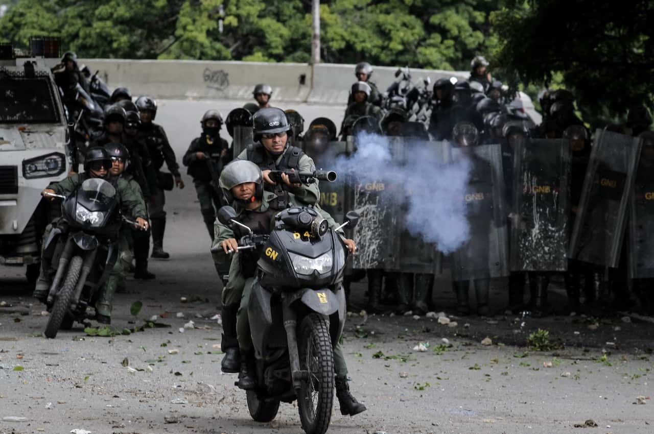 Members of the Bolivarian National Guard (GNB) on their motorbike confront a group of demonstrators during a protest against the government in Caracas (AAP)