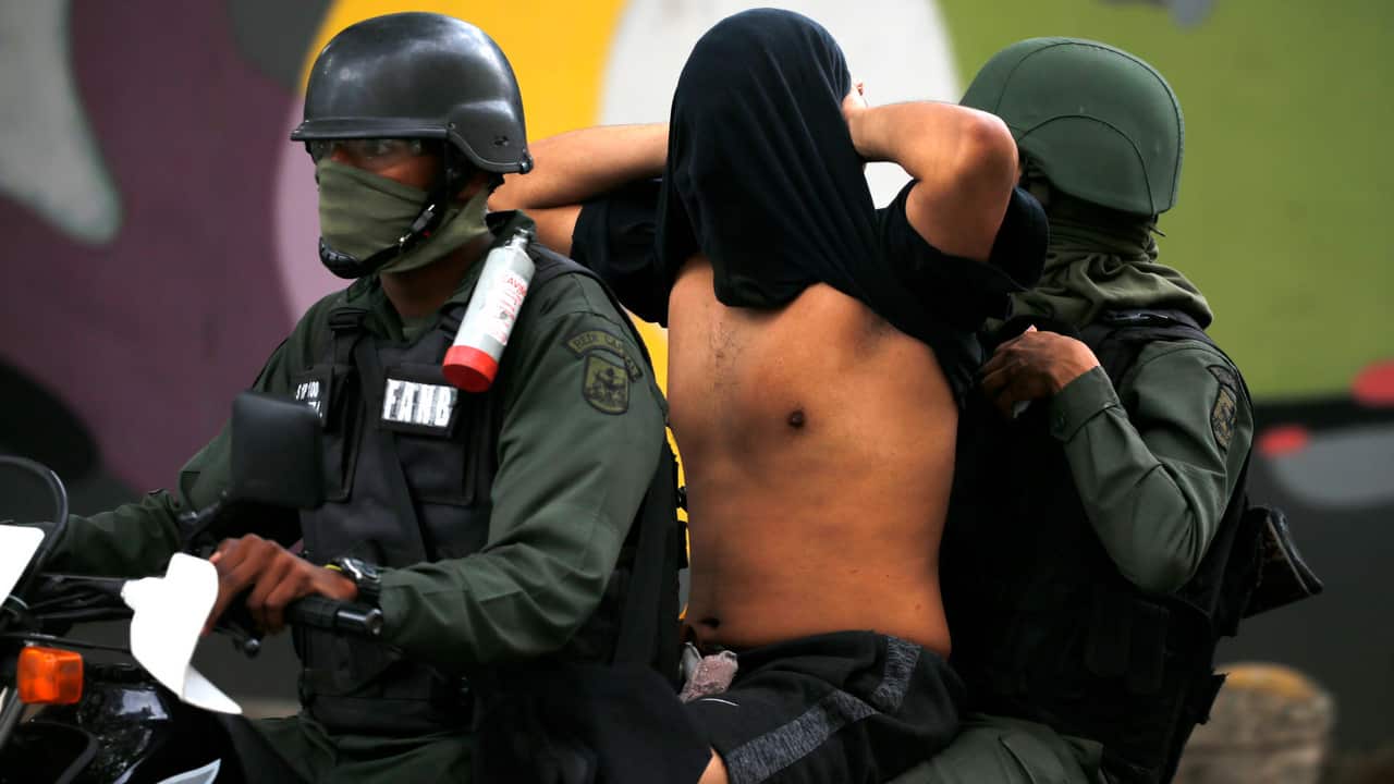 Venezuelan Bolivarian National Guard soldiers detain an anti-government protester, whose face they covered.