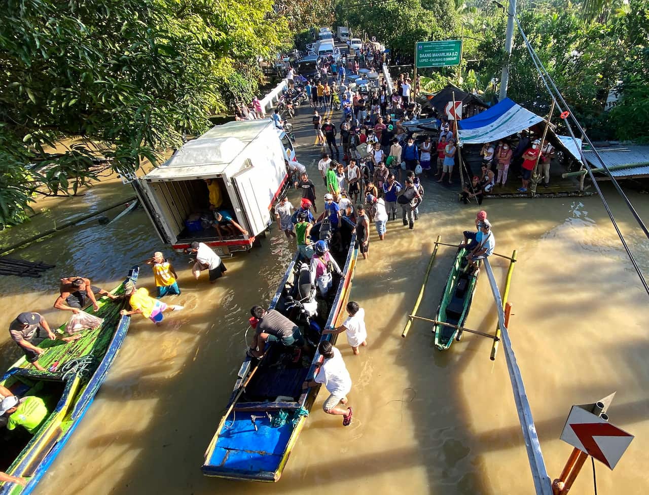 A crowd of stranded motorists disembark from a boat on a flooded road in the aftermath of Typhoon Vamco in the town of Lopez, Quezon province, Philippines.