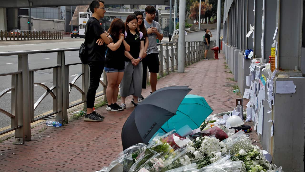Mourners offer prayer near the flowers on the site where a man fell to his death a day earlier after hanging a protest banner.