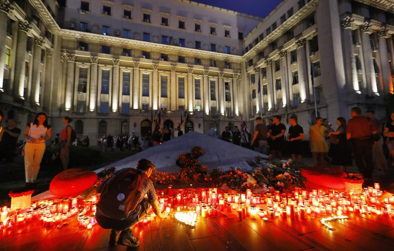 A Romanian young man kneels to light a candle at the end of a protest against the way Romanian authorities handled the kidnapping of a 15-years old girl