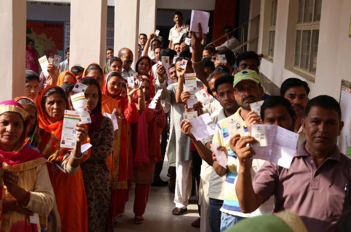 Indian voters hold their voting slips as they stand in a queue to cast their votes.