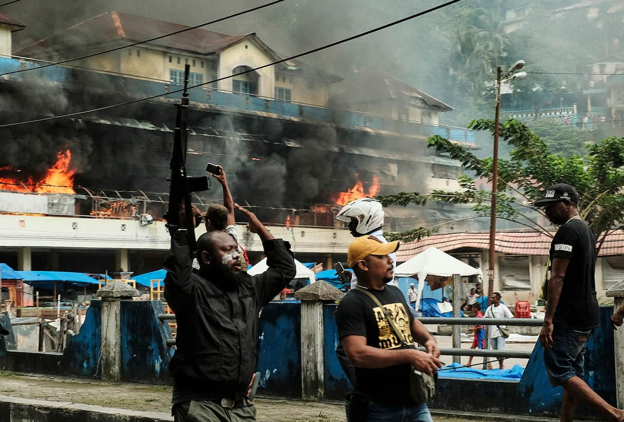A Papuan police officer carries a riffle as he controls the crowd after protesters torched Buruni market during a violent protest in Fakfak, West Papua.