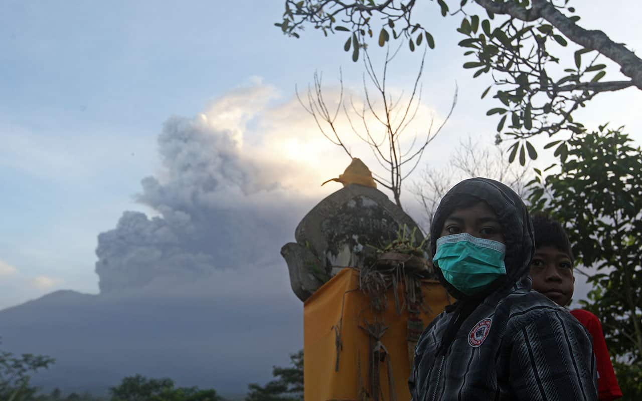 A girl wears mask as the Mount Agung volcano erupting in the background in Karangasem, Bali island, Indonesia, Sunday, November 26, 2017.