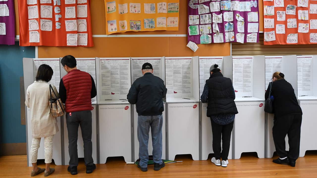 Five people writing on papers in a ballot booth.