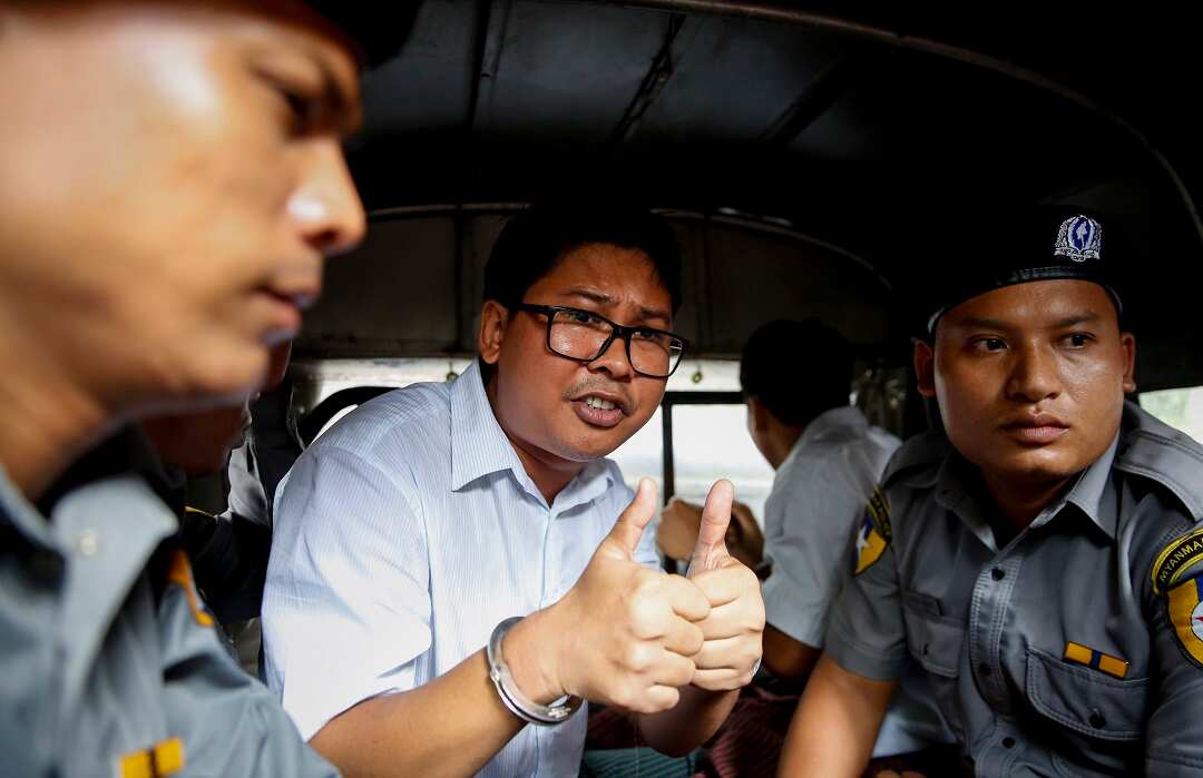 Reuters journalist Wa Lone tries to reassure onlookers as he's taken away in a police van after being sentenced to seven years' jail. 
