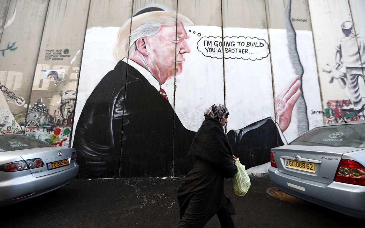 A woman walks past sprayed graffiti of US President Donald Trump is seen on the Israeli separation wall in the West Bank city of Bethlehem, 6 December 2017. 