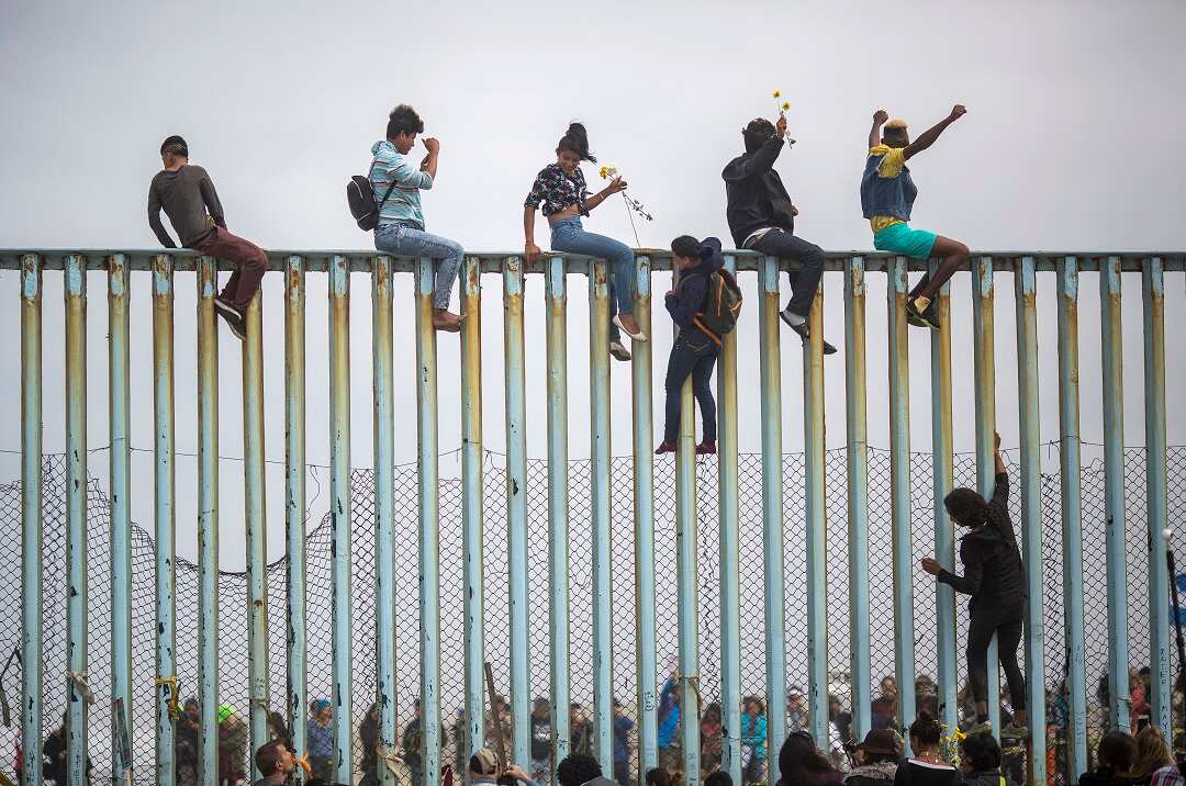 Members of a caravan of Central American asylum seekers scale a wall at the US-Mexico border.  The president has doubled down on his vow to fence off the border