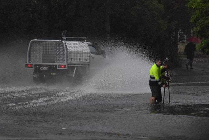 Council workers clear a drain as a car drives through floodwaters on Railway Terrace in Lewisham.