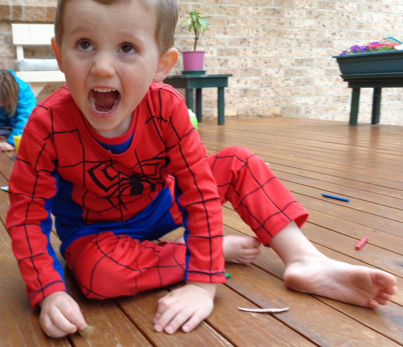A little boy wearing a Spiderman suit sitting on a wooden floor.