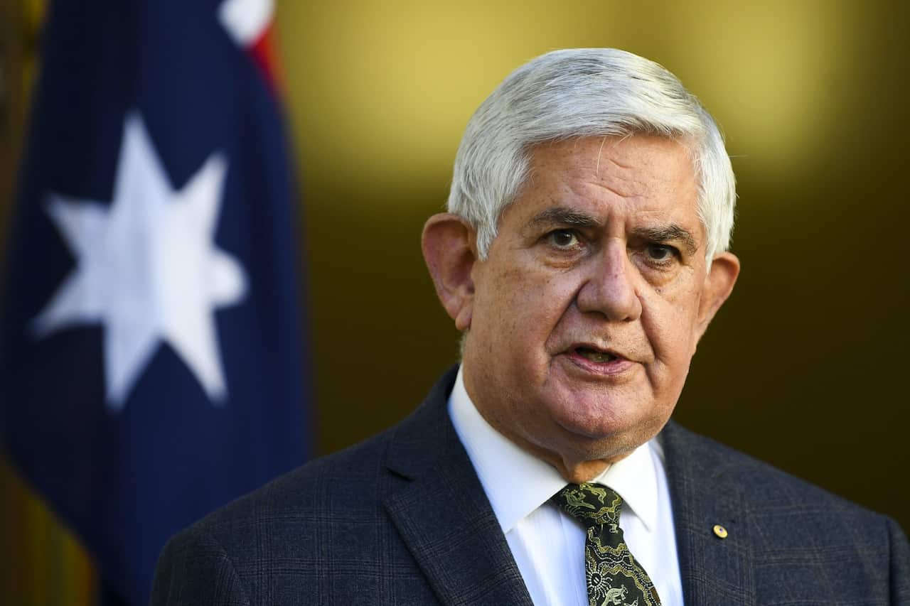 Ken Wyatt in front of an Australian flag.