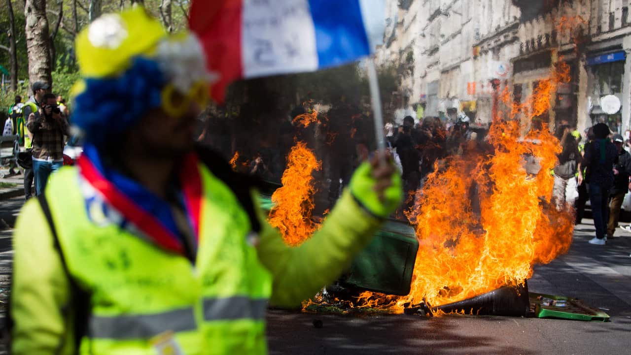 Yellow vest holding a french flag in front of a fire during the demonstration.