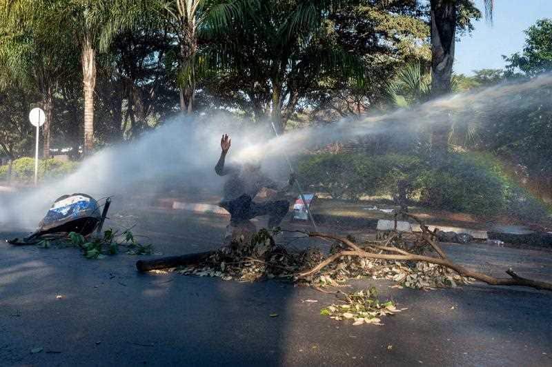 A protester is hit in the face by a stream of water as riot police turn water cannons on people.