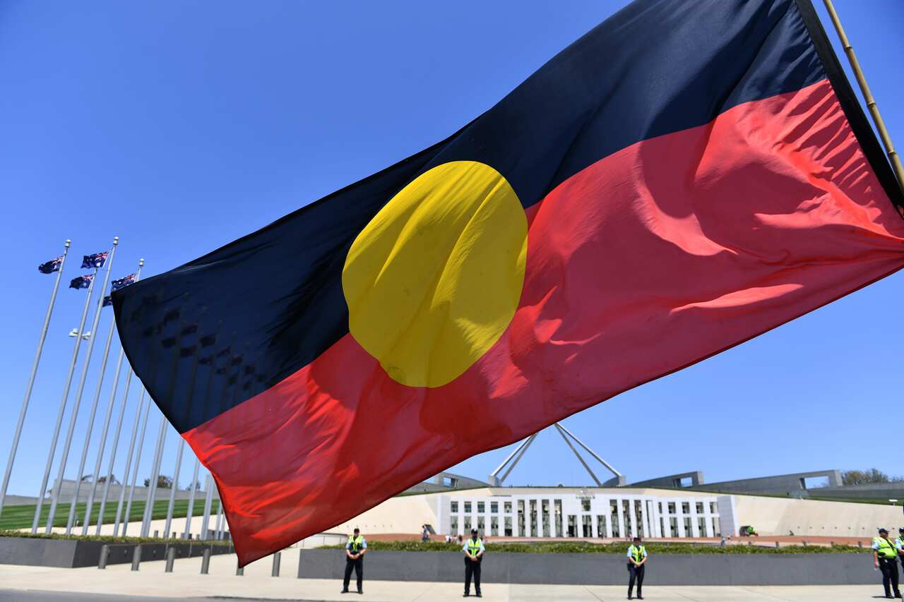A marcher holds a flag as he protests for Aboriginal rights on Australia Day at Parliament House in Canberra, Sunday, January 26, 2020. (AAP) 