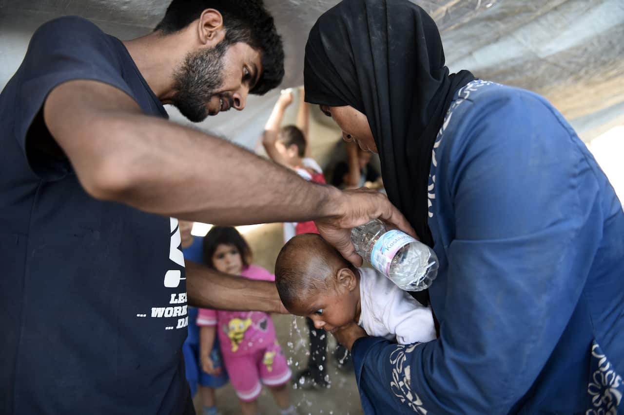 Parents from Syria use water to cool their baby as they wait to cross the border from the northern Greek town of Idomeni to southern Macedonia (AAP)