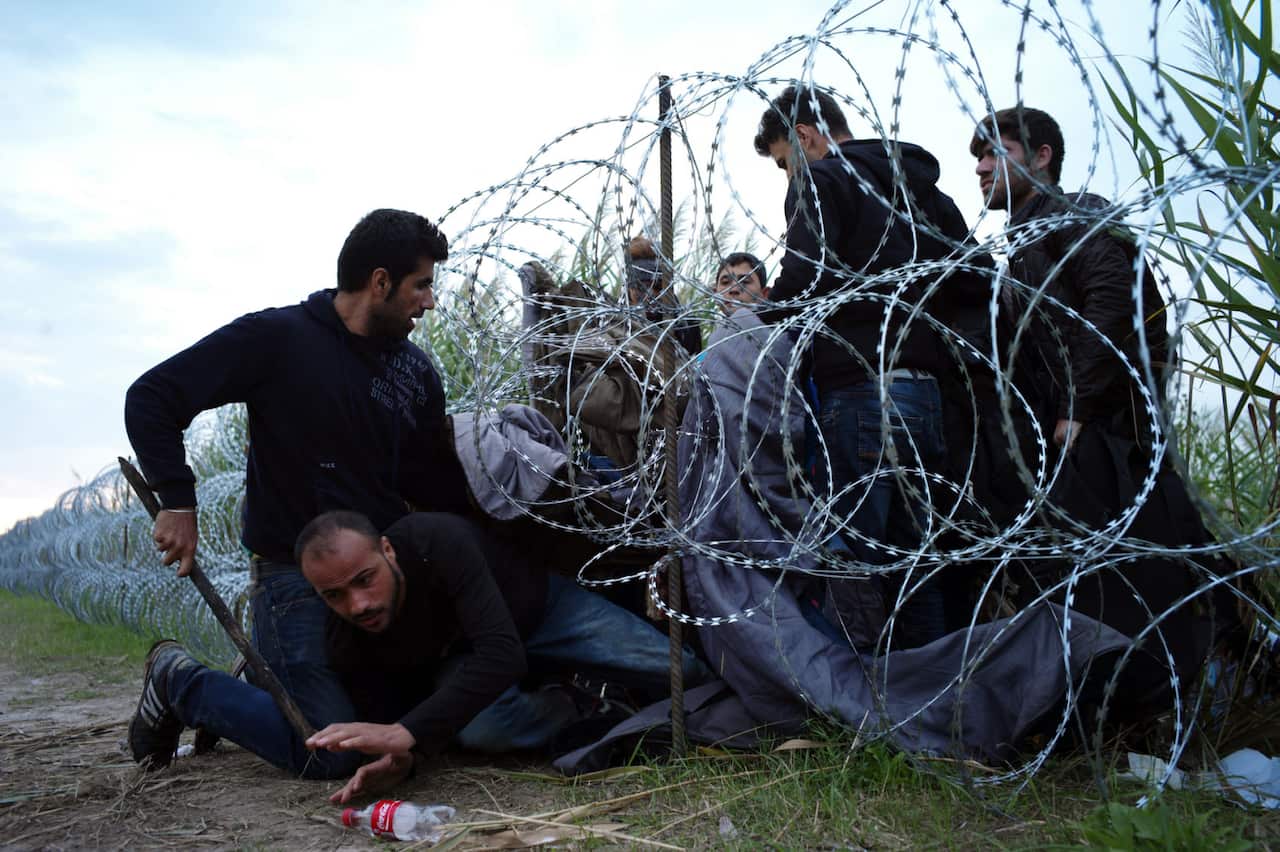 Syrian refugees cross into Hungary underneath the border fence on the Hungarian